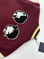 Maroon varsity jacket close-up with two dog-head patches and striped cuff ribbing.