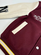 Varsity jacket close-up: maroon front with white sleeve, ribbed collar, striped hem.
