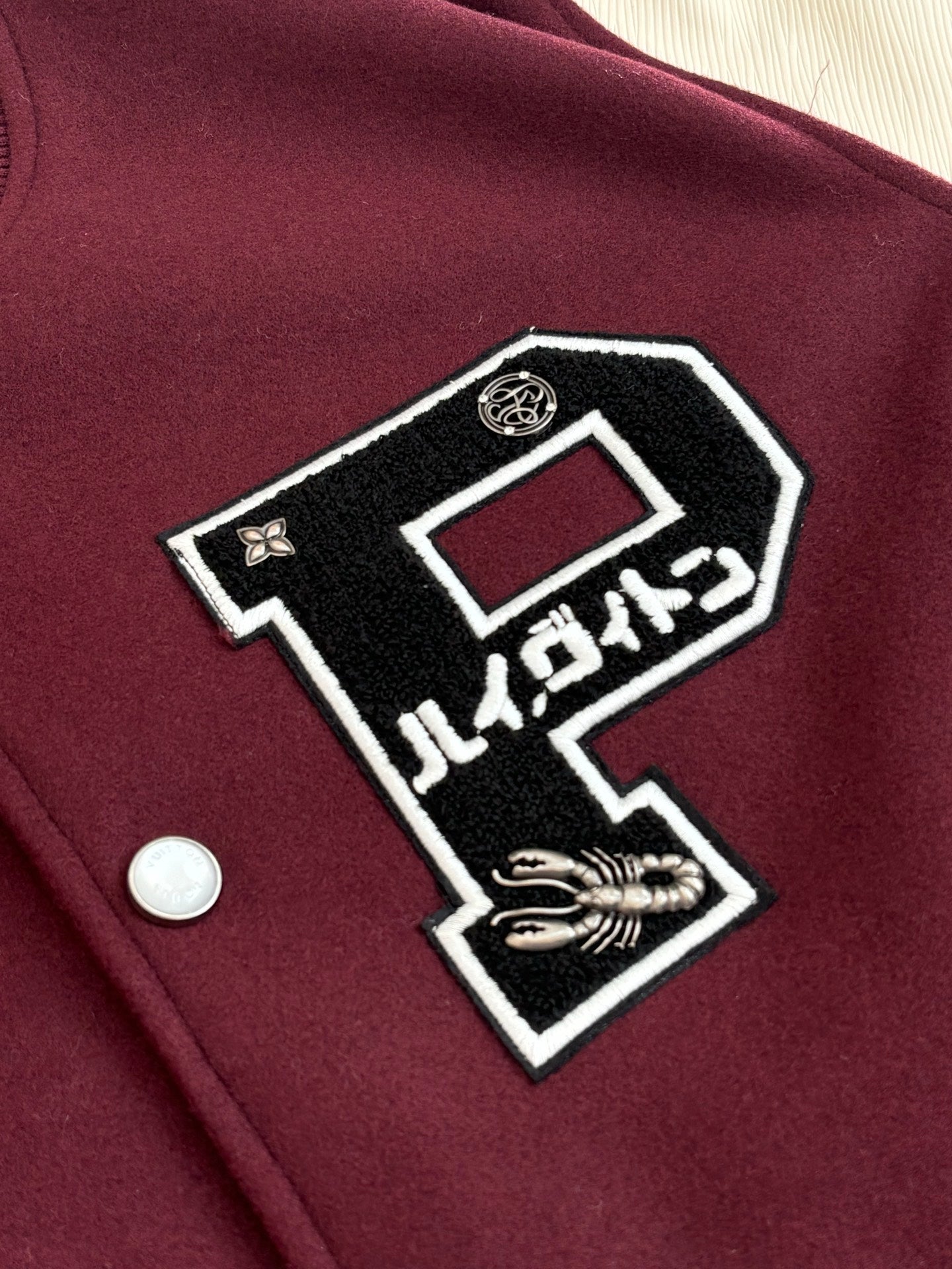 Maroon varsity jacket front patch detail with black-and-white graphic and button.