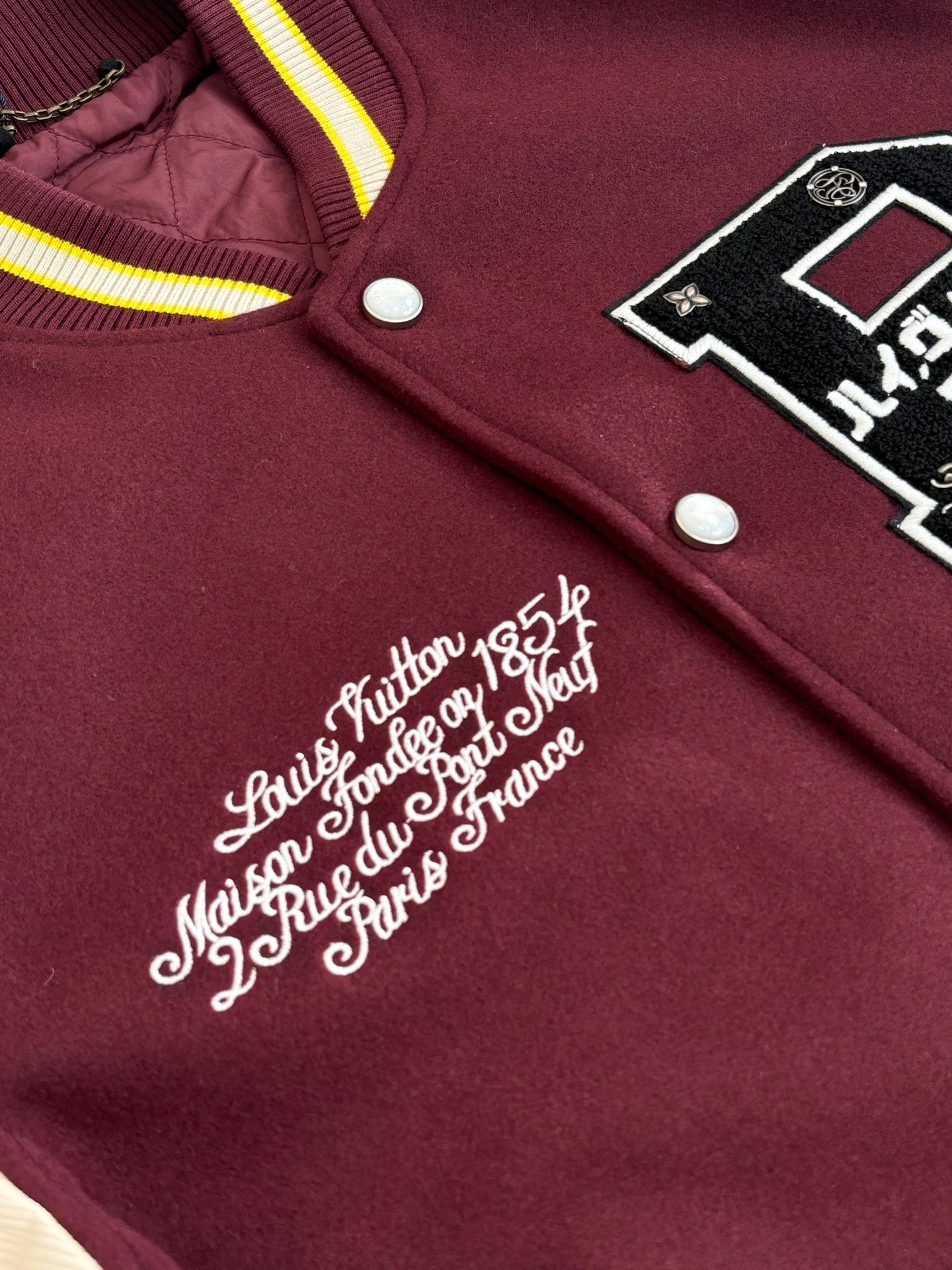 Maroon varsity jacket with cursive embroidery, snap buttons, and striped collar trim.