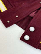 Maroon varsity jacket cuff and button detail with ribbed hem and striped side trim.