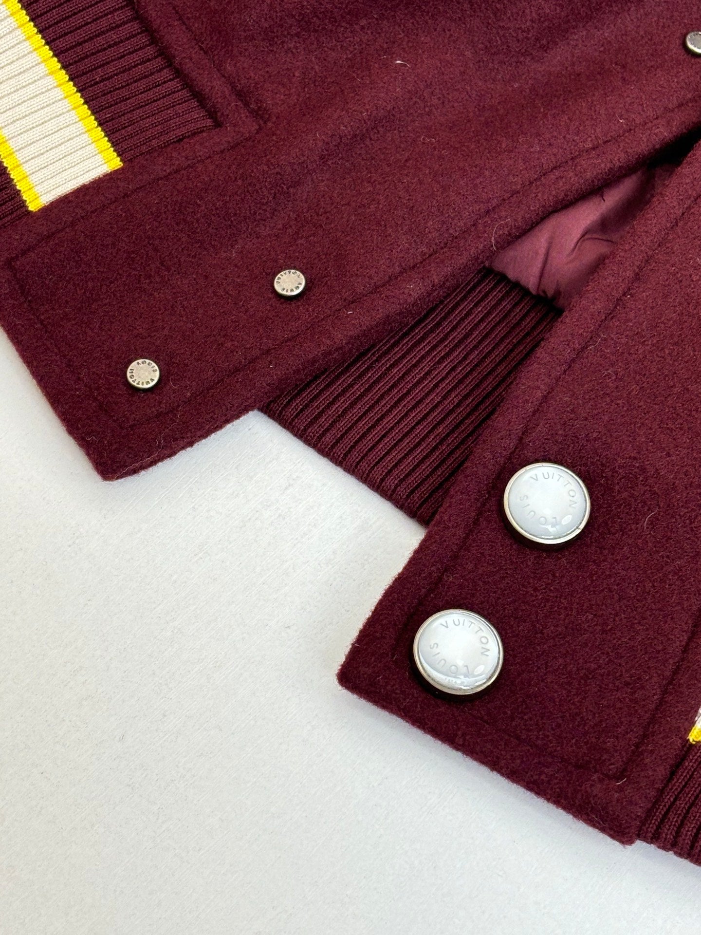 Maroon varsity jacket cuff and button detail with ribbed hem and striped side trim.
