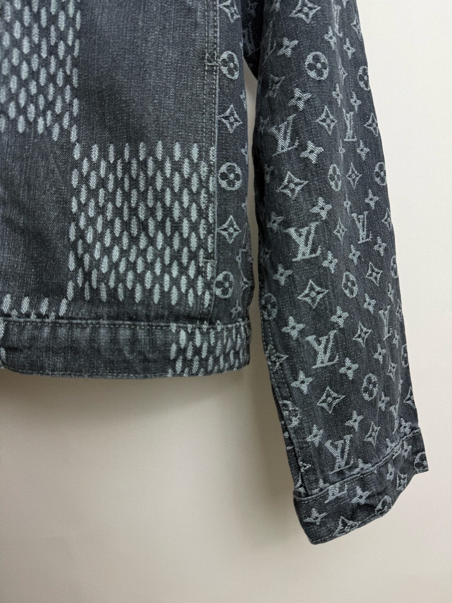 Dark denim jacket sleeve and hem with monogram print and stitched check pattern.