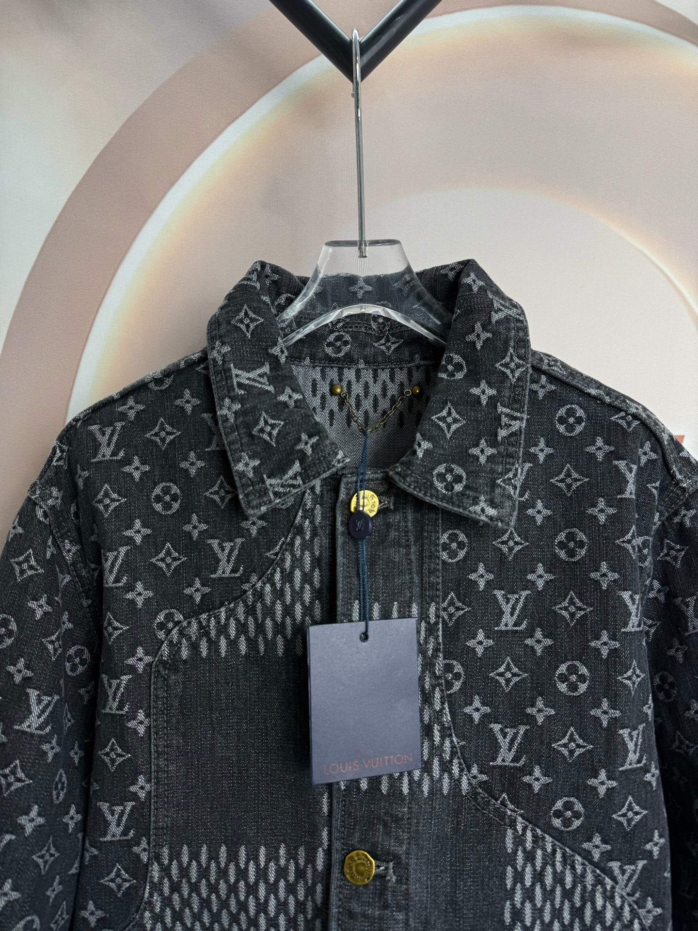 Dark denim jacket close-up with monogram pattern, snap buttons, and hanging tag.