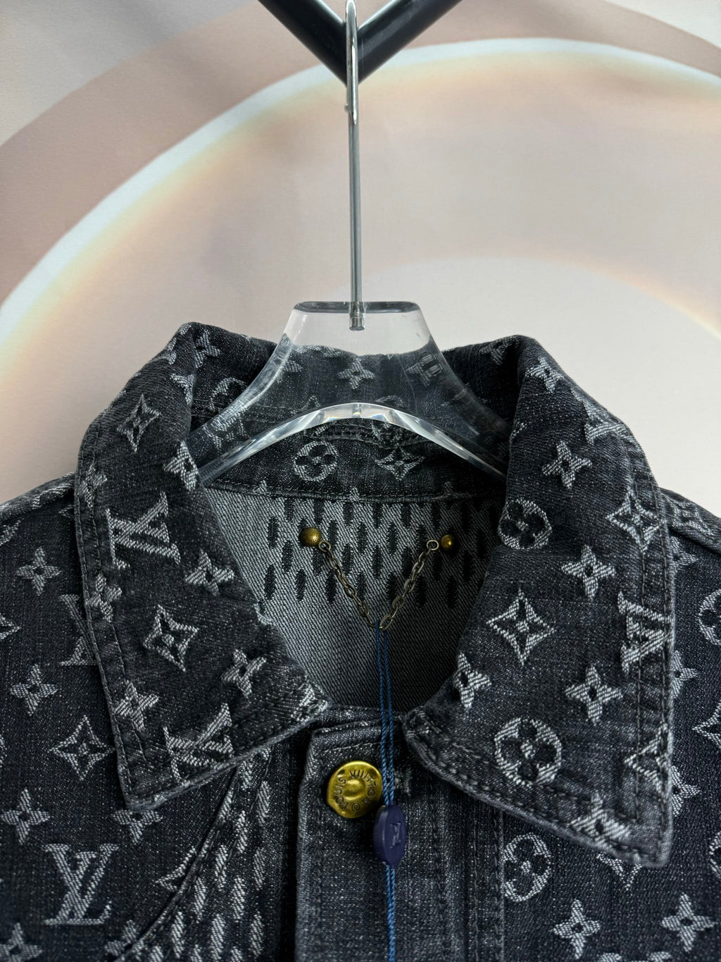 Dark denim jacket front close-up with monogram print, snap buttons, and hanging tag.