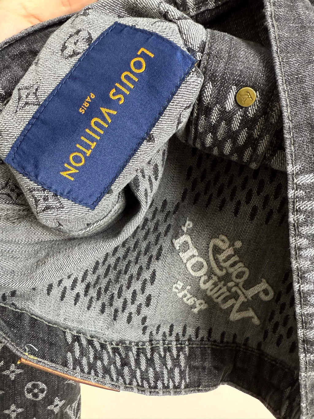 Denim jacket interior close-up with fabric tag reading "Louis Vuitton".