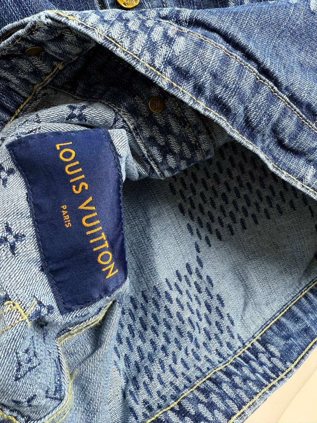 Blue denim jacket interior label with gold text reading "Louis Vuitton"