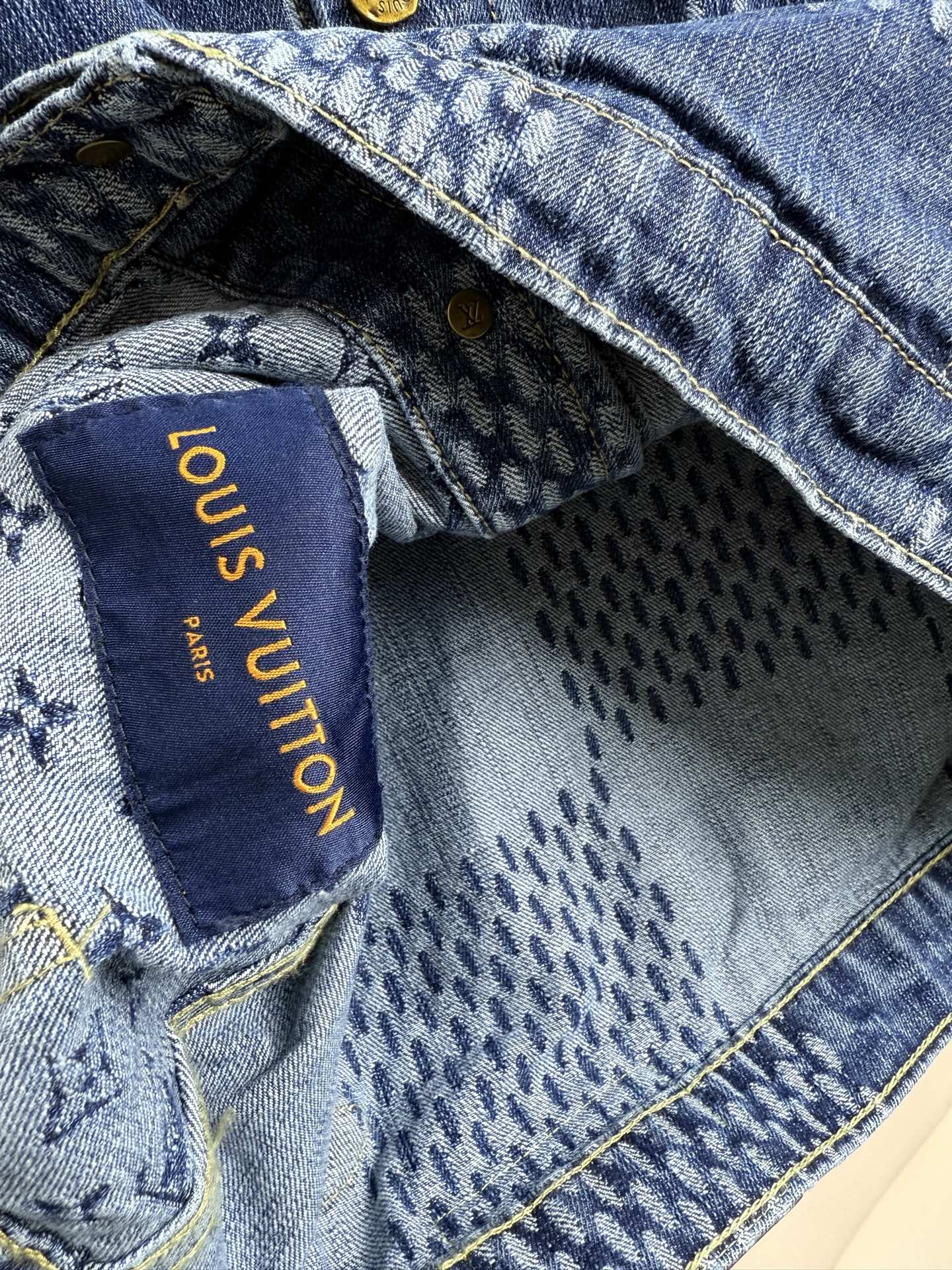 Blue denim jacket interior label with gold text reading "Louis Vuitton"