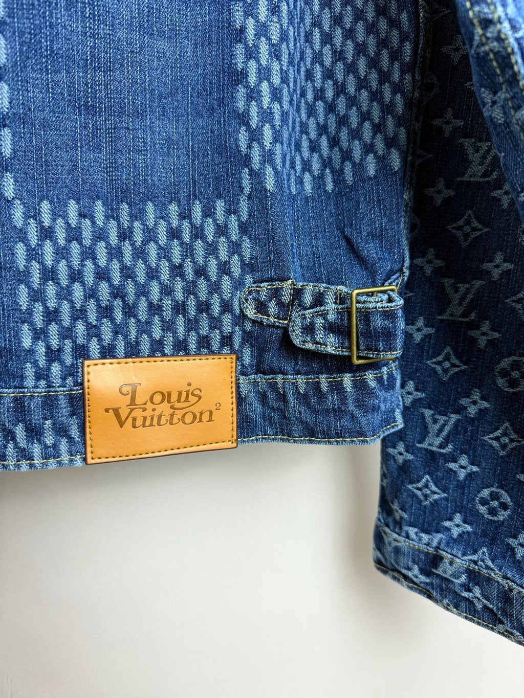 Blue denim jacket close-up of tan "Louis Vuitton" brand label with button-tab
