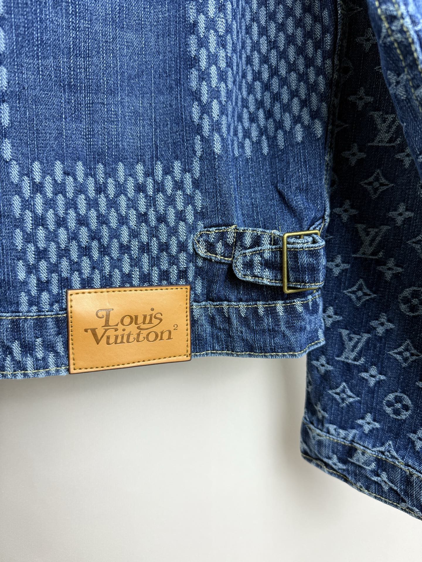 Blue denim jacket close-up of tan "Louis Vuitton" brand label with button-tab
