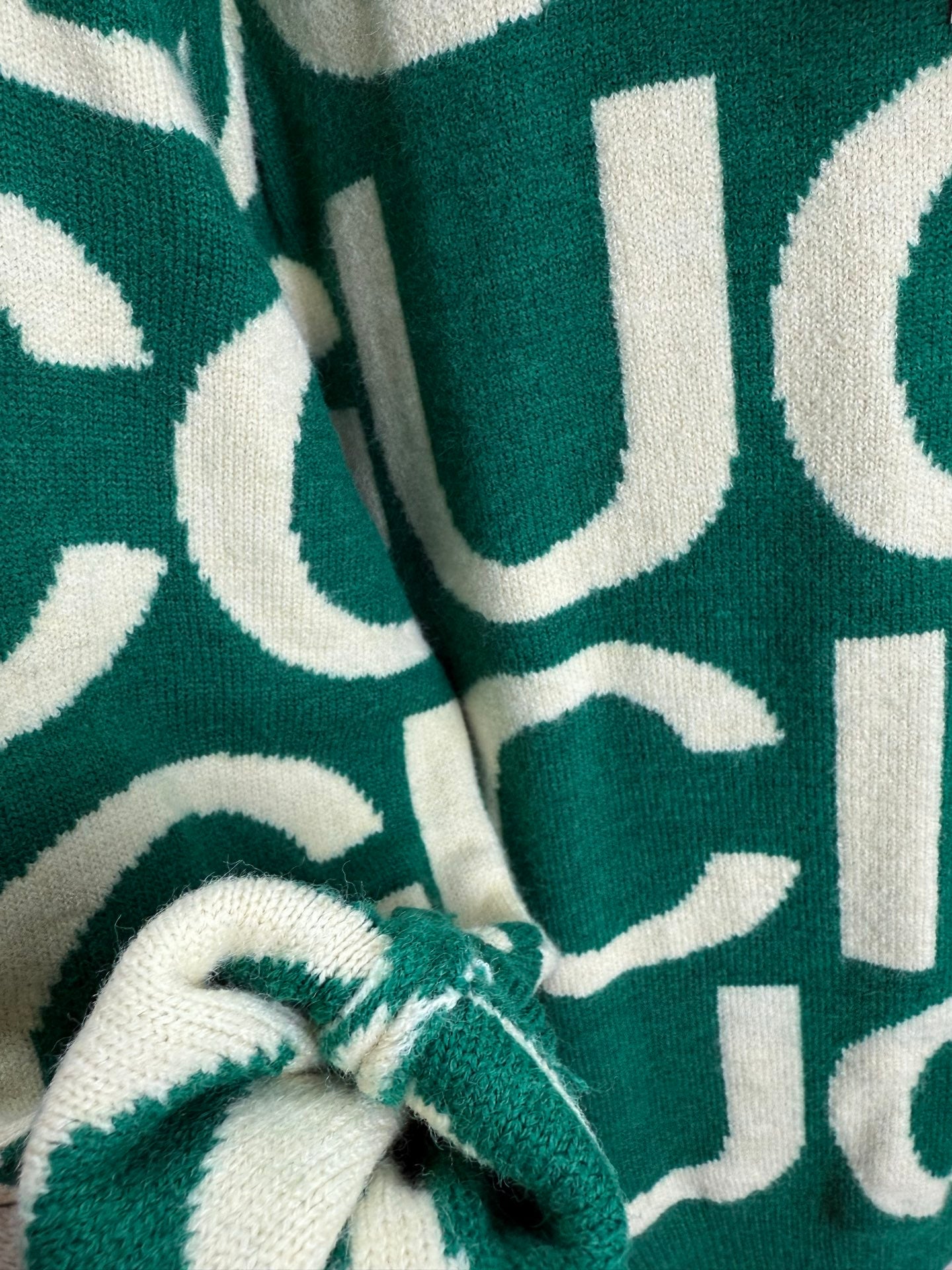 Knit sweater close-up, green fabric with cream lettering pattern