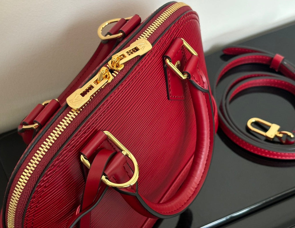 Louis Vuitton red handbag side detail with gold-tone zipper pull and D-ring