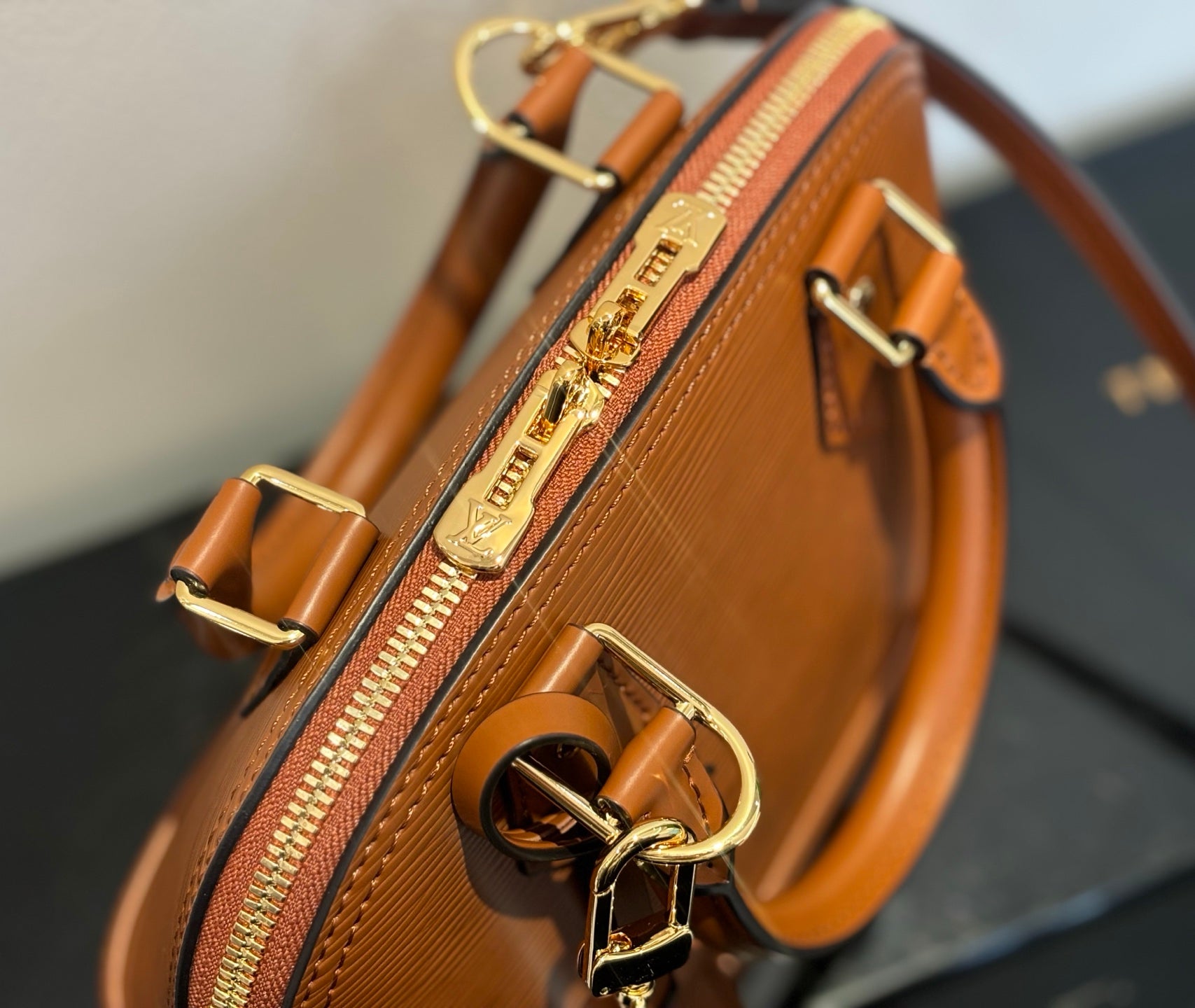 Side view of tan leather handbag with zip pocket and gold clasp detail, crossbody strap