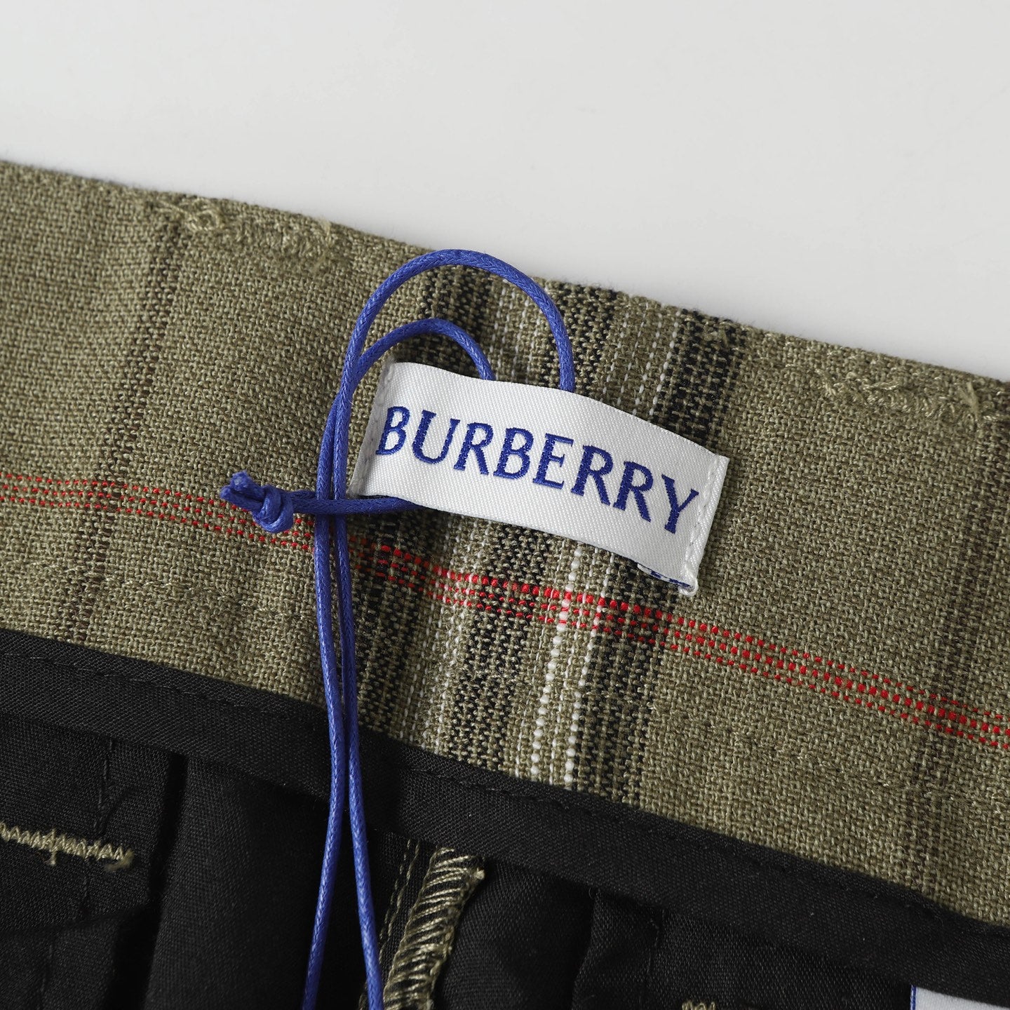 Woven brand label on olive plaid pants with blue drawstring tie
