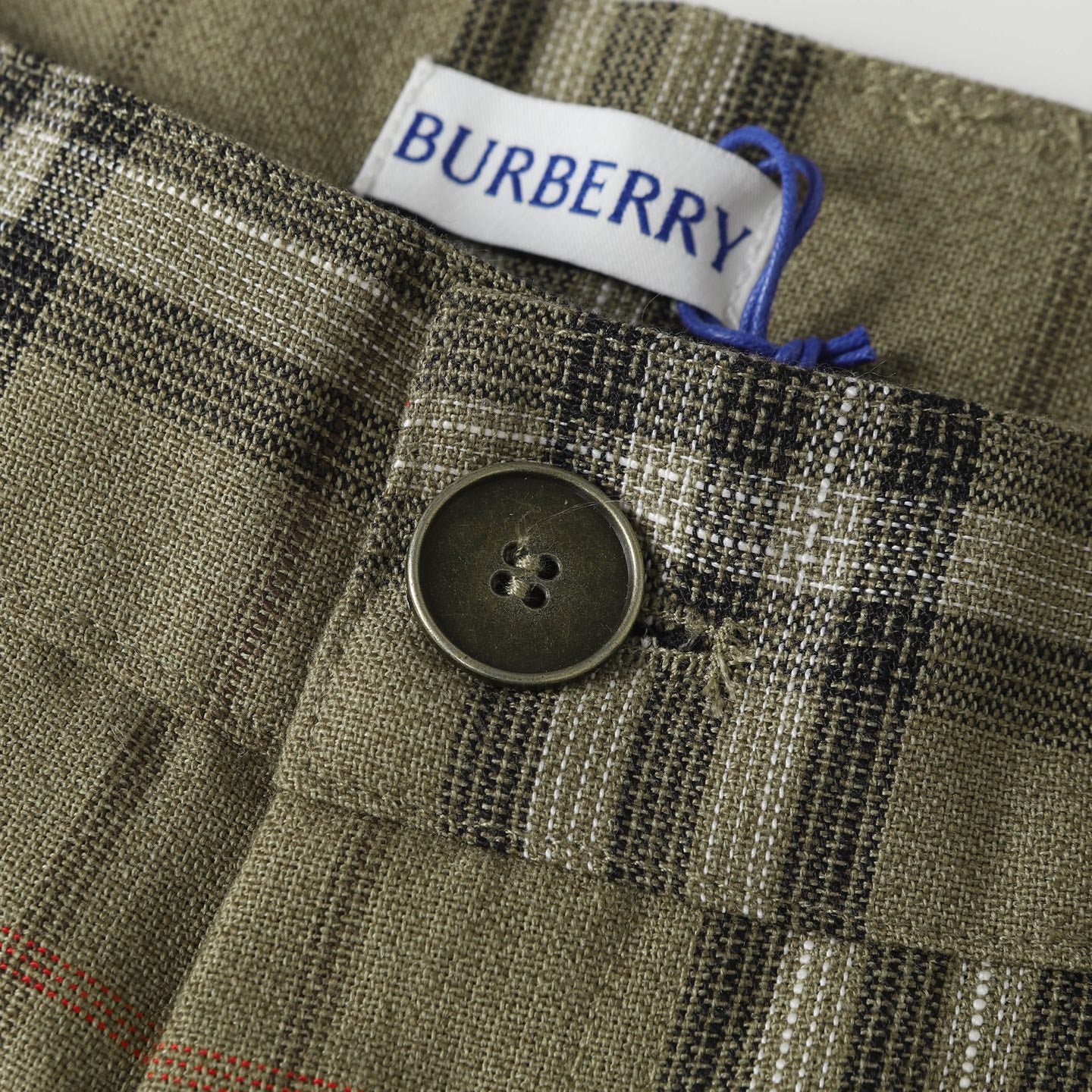 Close-up of plaid pants button and waist label with blue drawstring