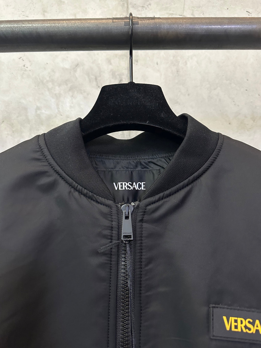 Black Versace bomber jacket close-up: stand collar, zipper, and chest logo patch
