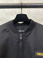 Black Versace bomber jacket close-up: stand collar, zipper, and chest logo patch