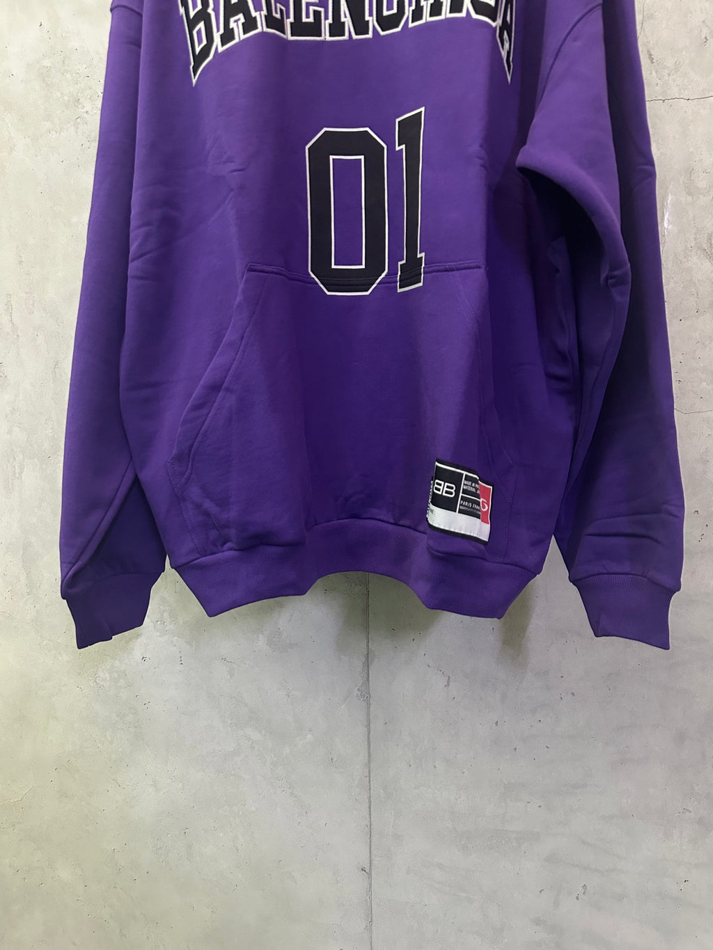 Purple Balenciaga hoodie with '01' graphic and small flag patch near hem