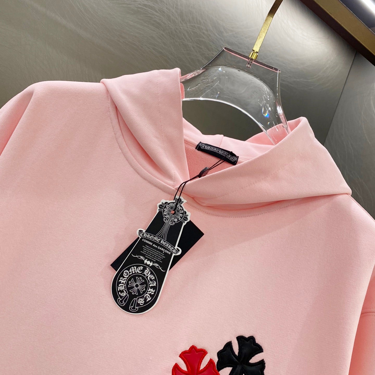 Pink hoodie with hood, black hanging tag, and red and black applique