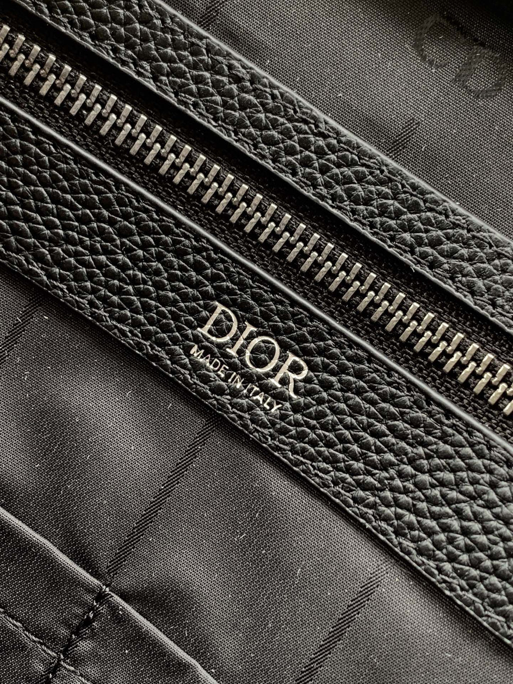 Black leather zipper pouch with Dior embossed text on fabric