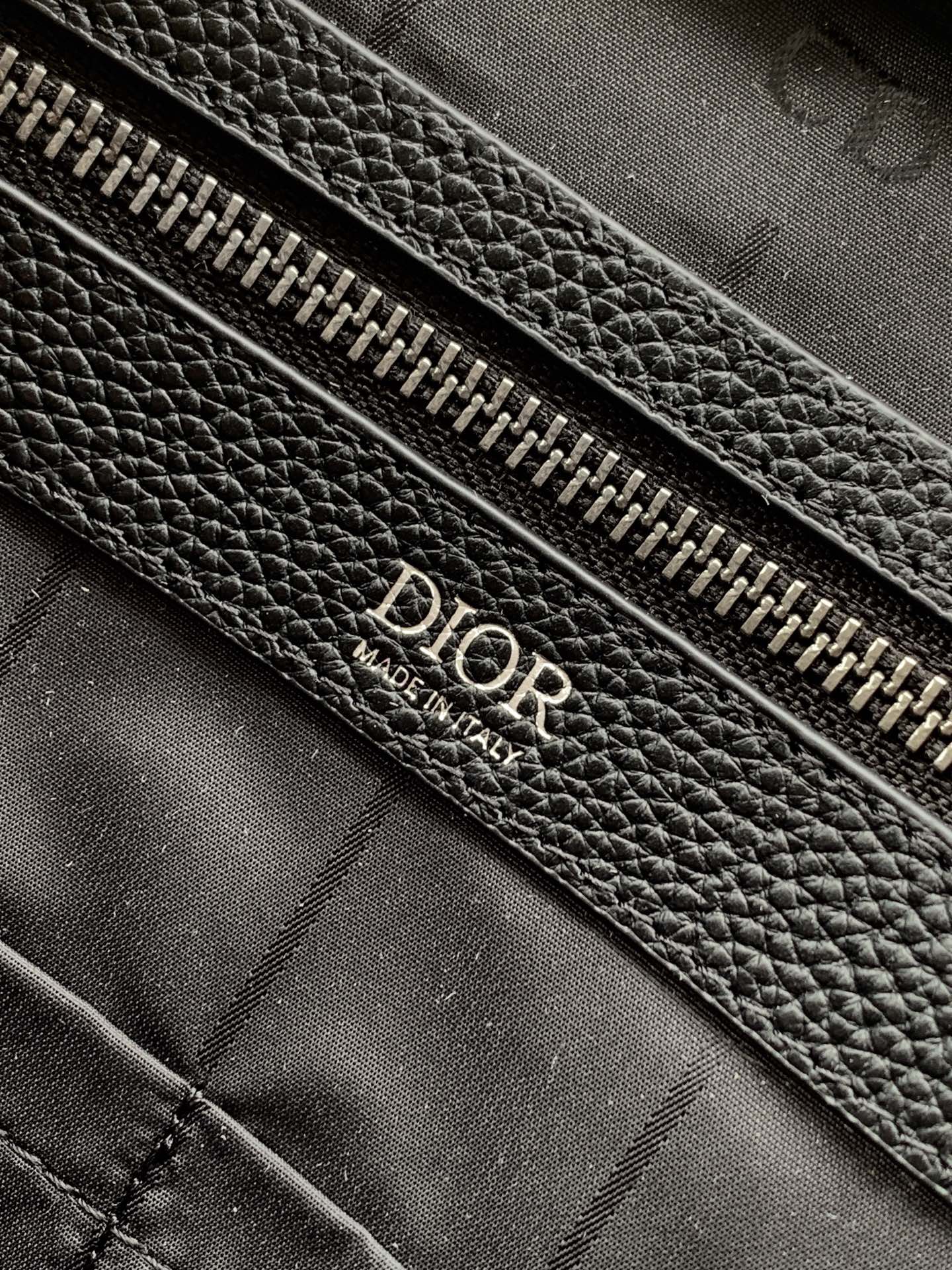 Black leather zipper pouch with Dior embossed text on fabric