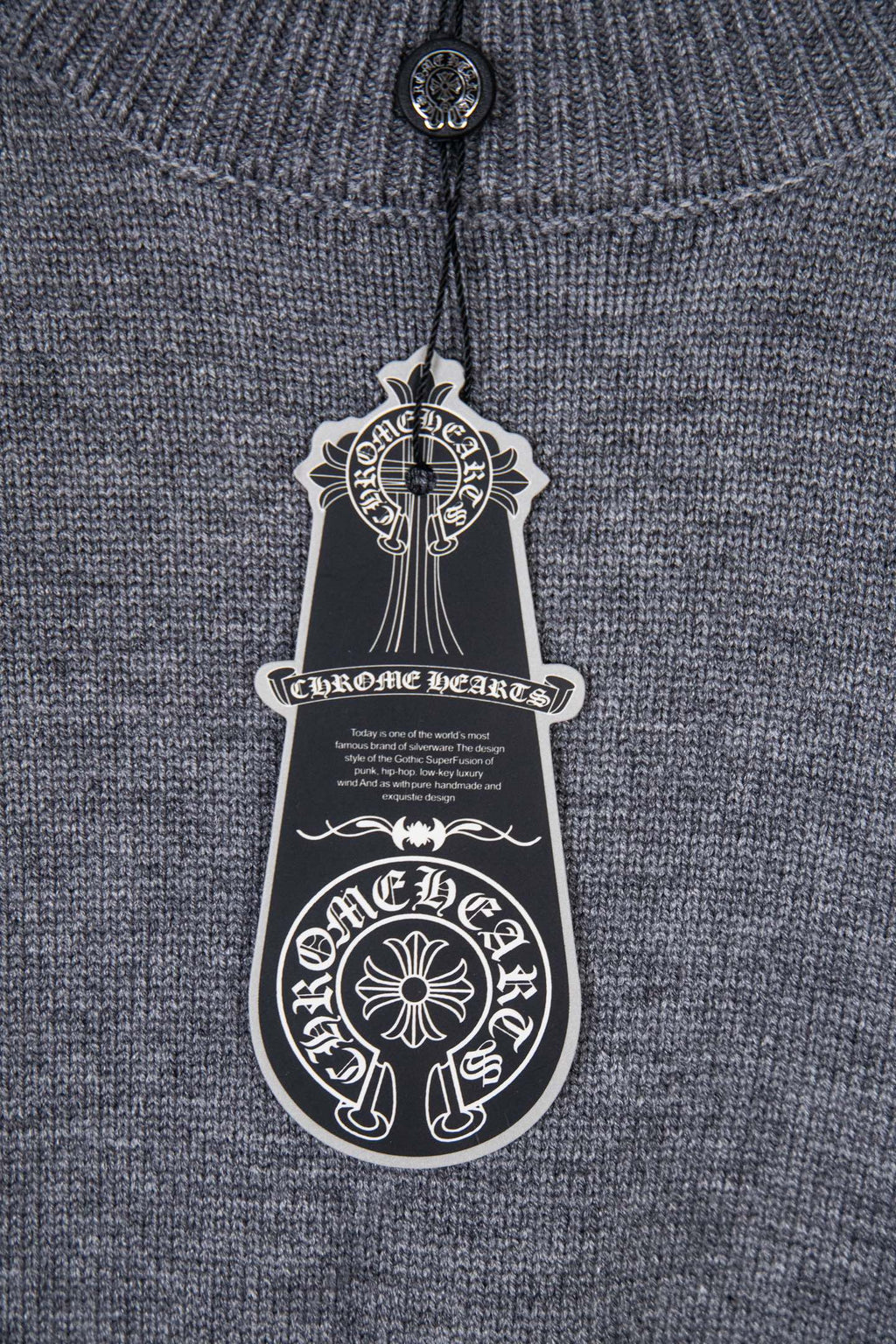 Gray knit sweater with hanging black logo tag at the neckline