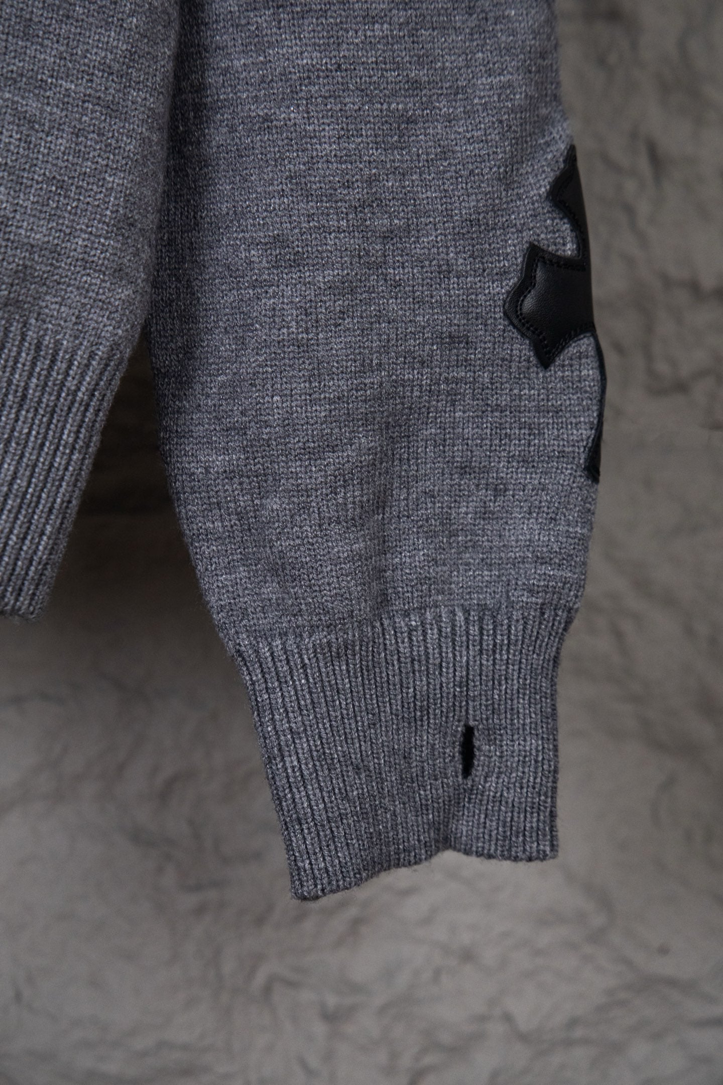 Gray knit sweater close-up of lower front with ribbed hem and small black detail