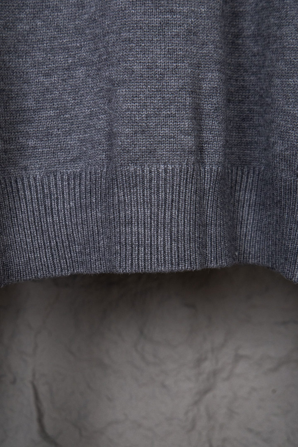 Gray knit sweater sleeve area with ribbed cuff and side seam visible