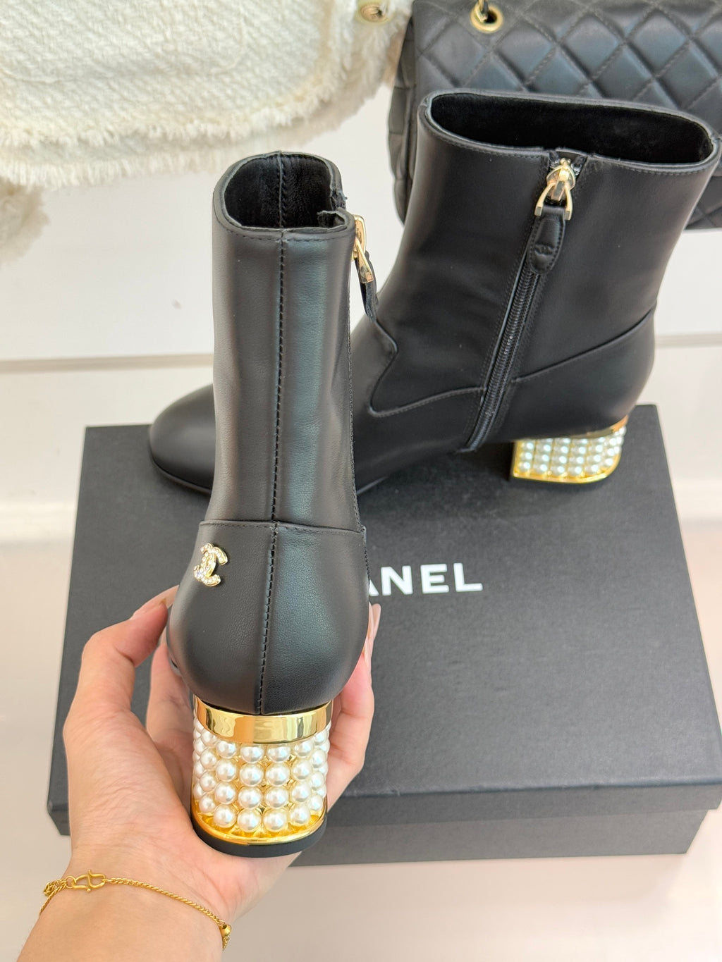 Black leather ankle boots on box, one held up, gold zipper pull and jeweled heel