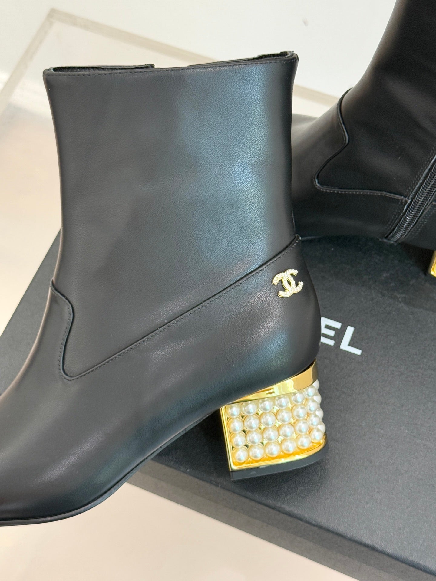 Black leather ankle boot with gold Chanel logo and jeweled block heel detail
