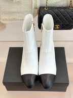 Pair of white ankle boots with black toe, zip closure, and gold studded heel