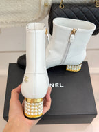 White ankle boots with gold studded heels, side zippers, on a box
