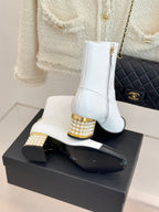 White ankle boots with black toe, gold studded heels, shown on a display box