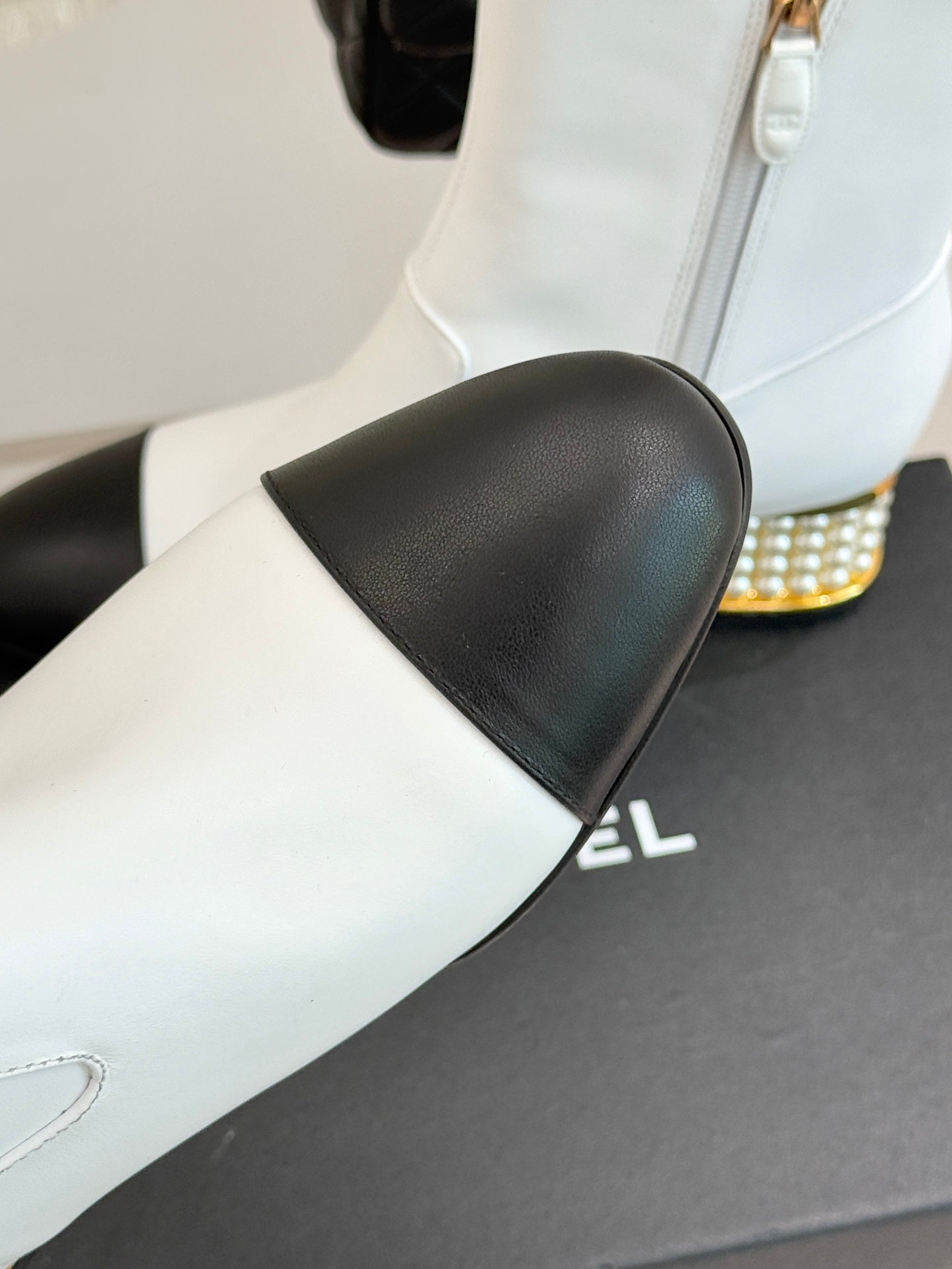 White ankle boot with black leather toe panel and gold-studded heel