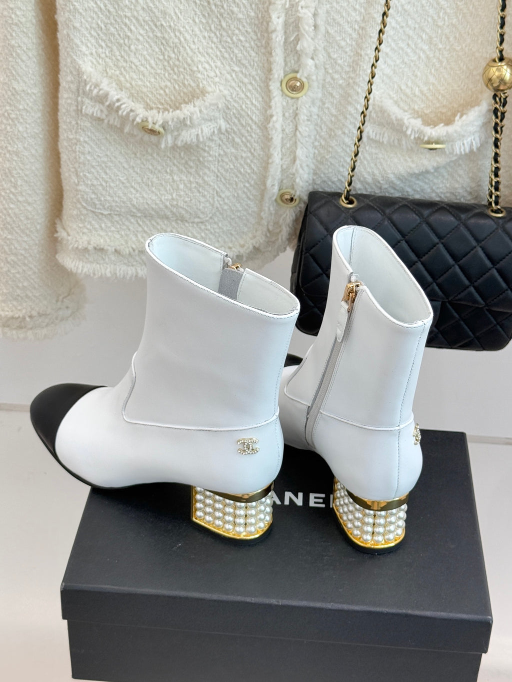 White ankle boots with gold logo charm, black toe cap, and studded heel