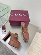 Brown Gucci ladies platform mules with gold buckle hardware, shown on white display