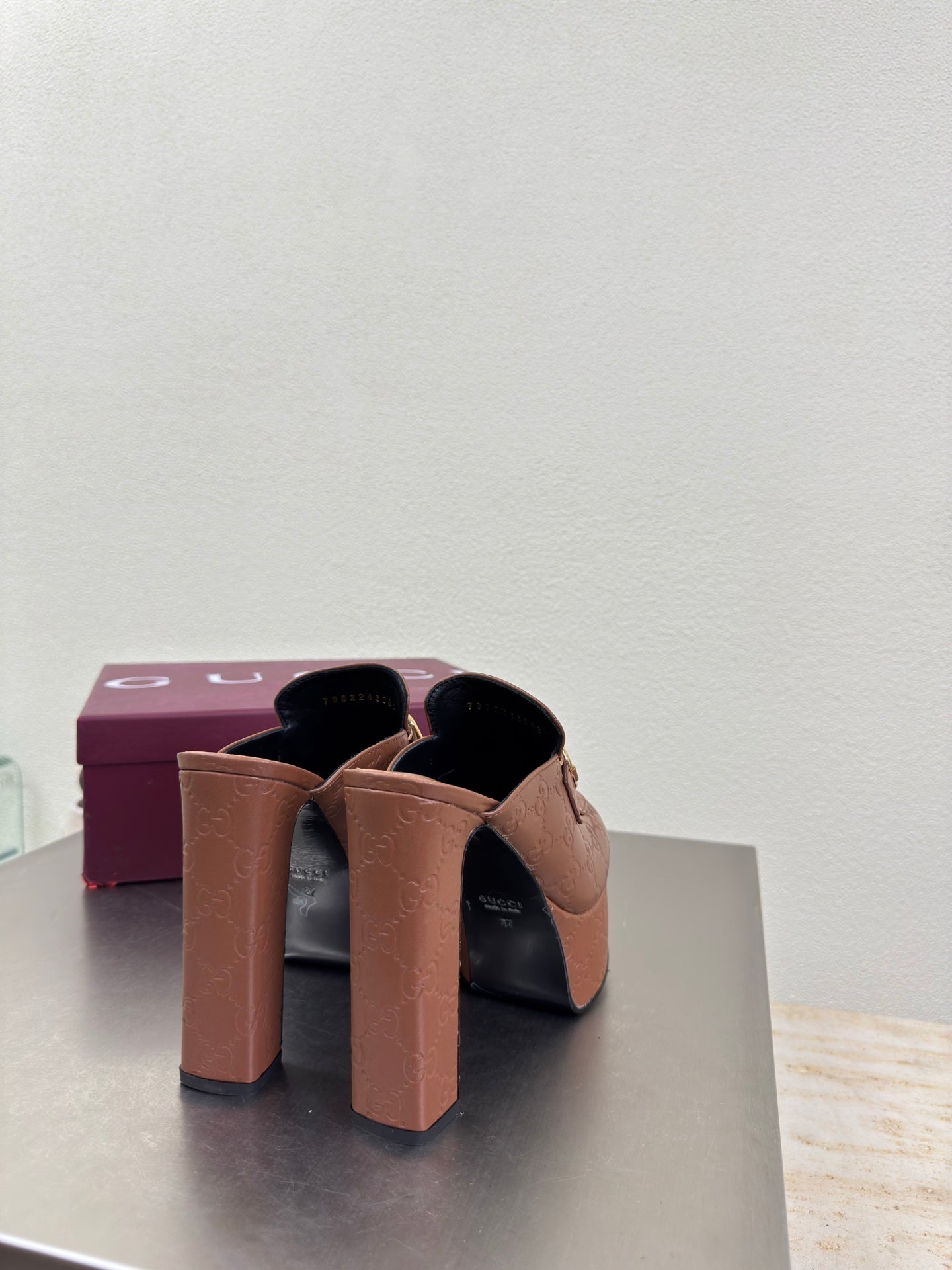 Brown Gucci platform mules with tall block heels and logo texture, rear angle