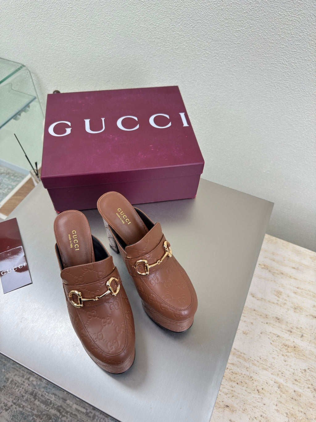 Brown Gucci ladies platform mules with gold buckle hardware and logo texture, pair shown