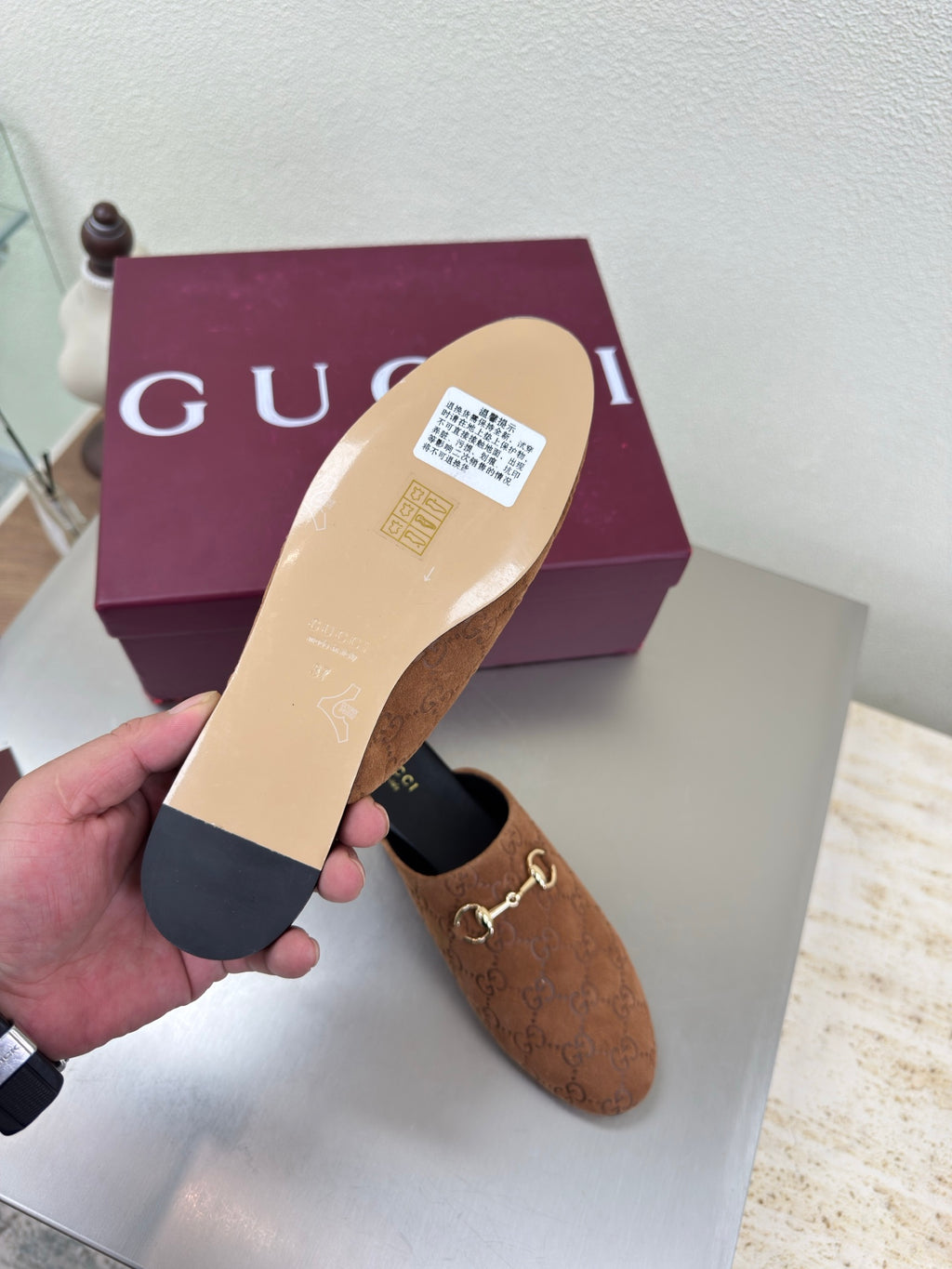 Women's brown monogram loafer held up; black sole and gold chain bit