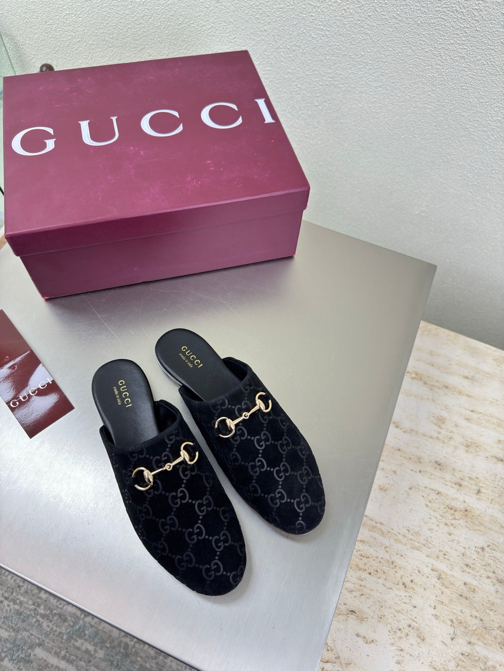 Black Gucci mules with GG logo print and gold horsebit detail, slip-on style