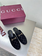 Black Gucci mules with GG logo print and gold horsebit detail, slip-on style