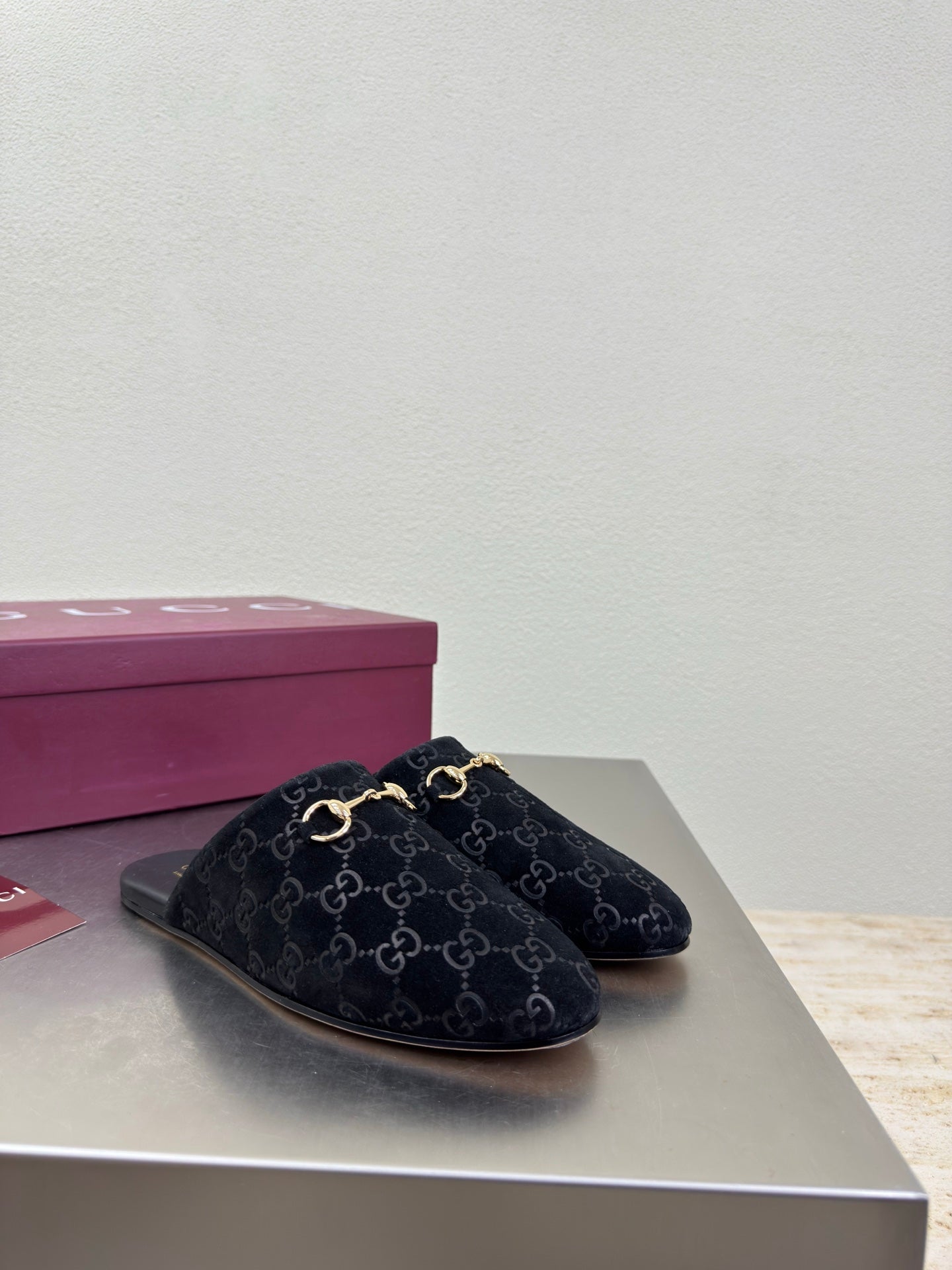 Black Gucci mule shoes with GG logo print and gold horsebit detail, side view