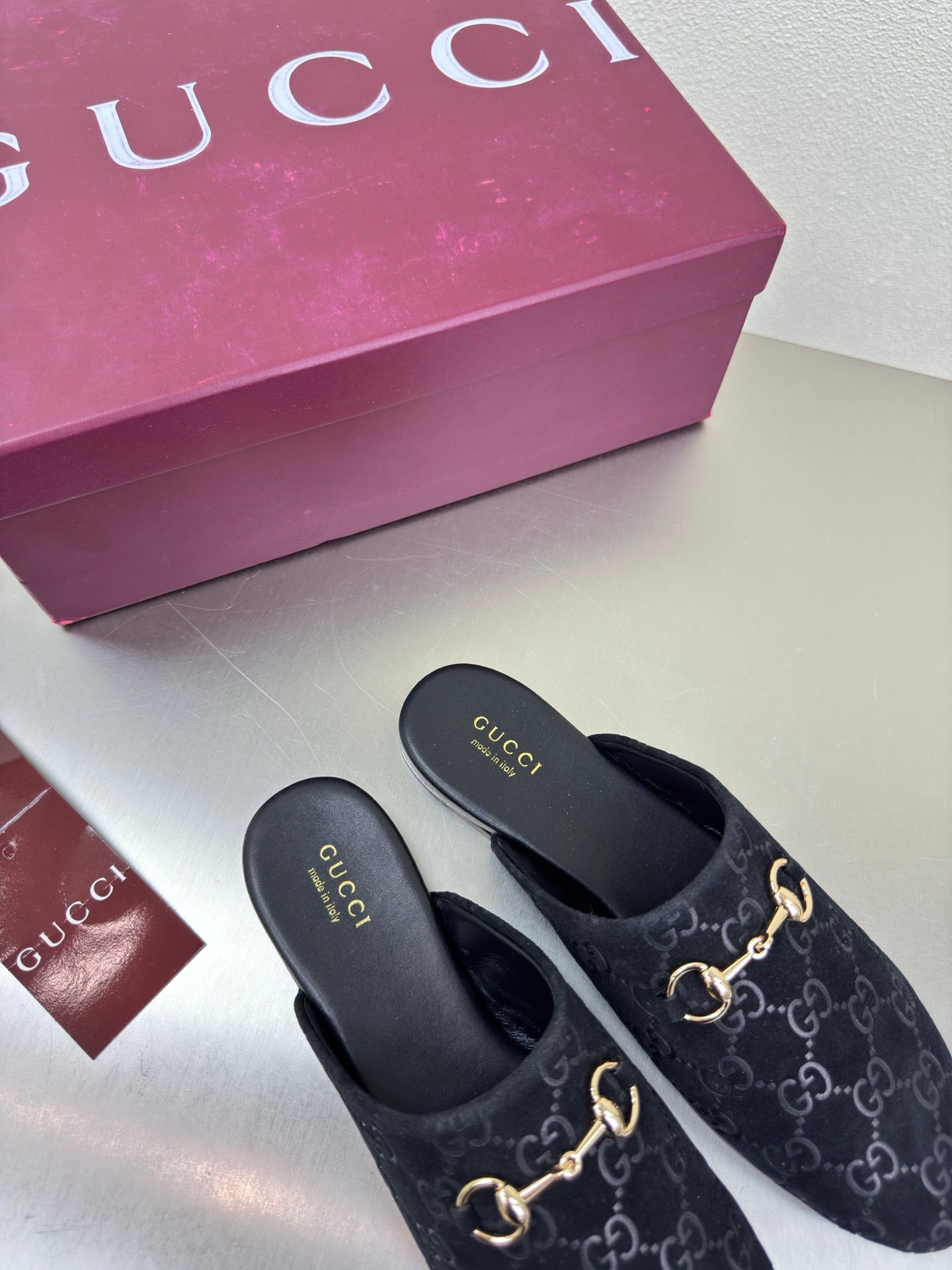 Black Gucci mules with GG logo print and gold horsebit detail, on white display