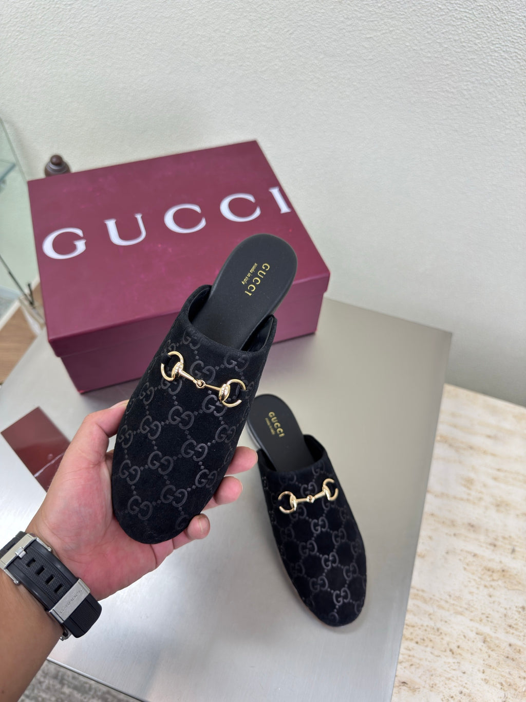 Black Gucci mules with GG logo print and gold horsebit detail, held in hand