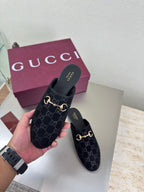 Black Gucci mules with GG logo print and gold horsebit detail, held in hand