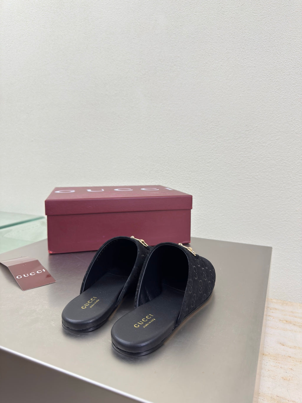Black Gucci mule shoes with GG logo print and gold horsebit detail, shoes on box