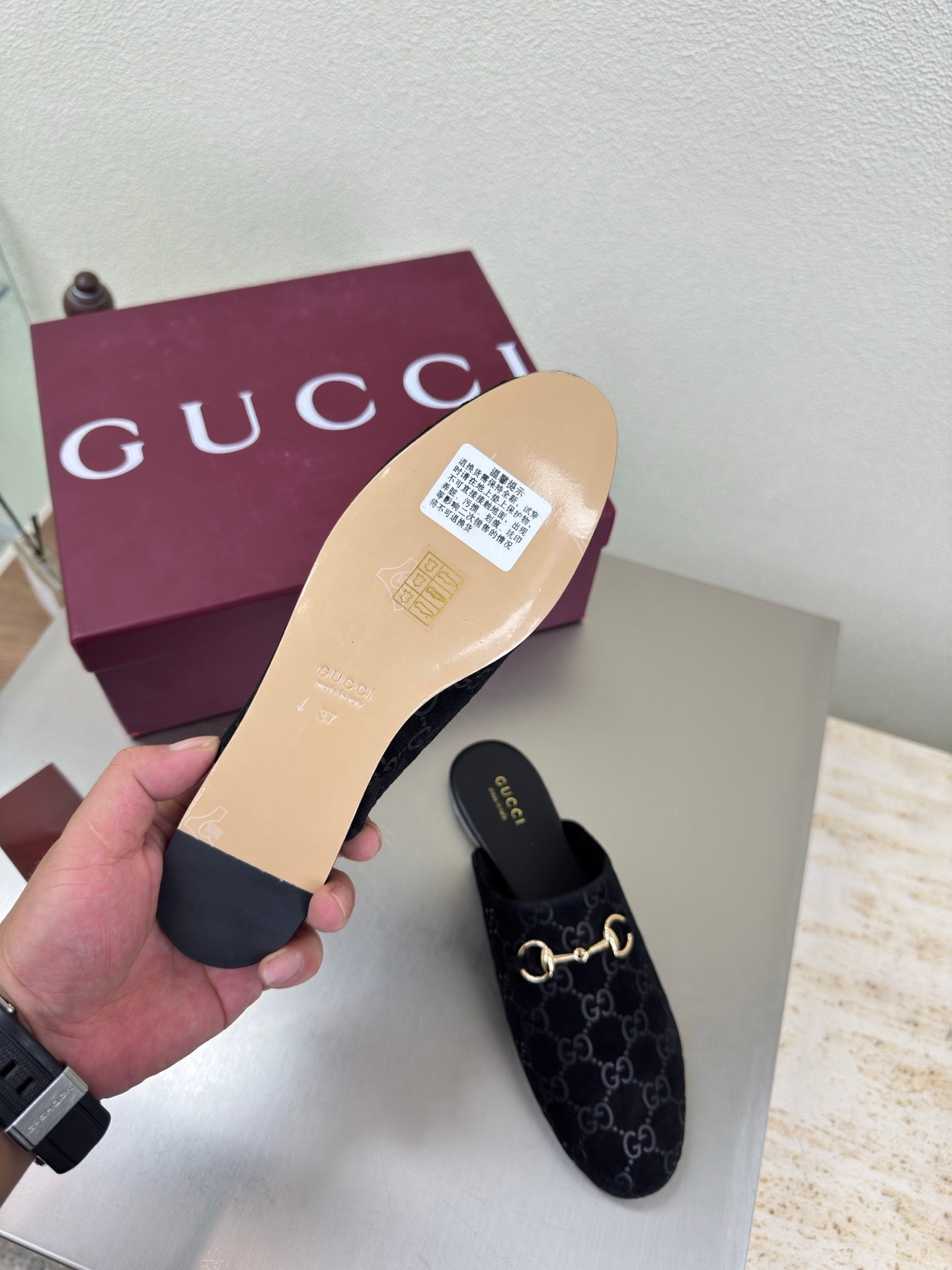 Black Gucci mule shoes with GG logo print and gold horsebit detail, outsole shown