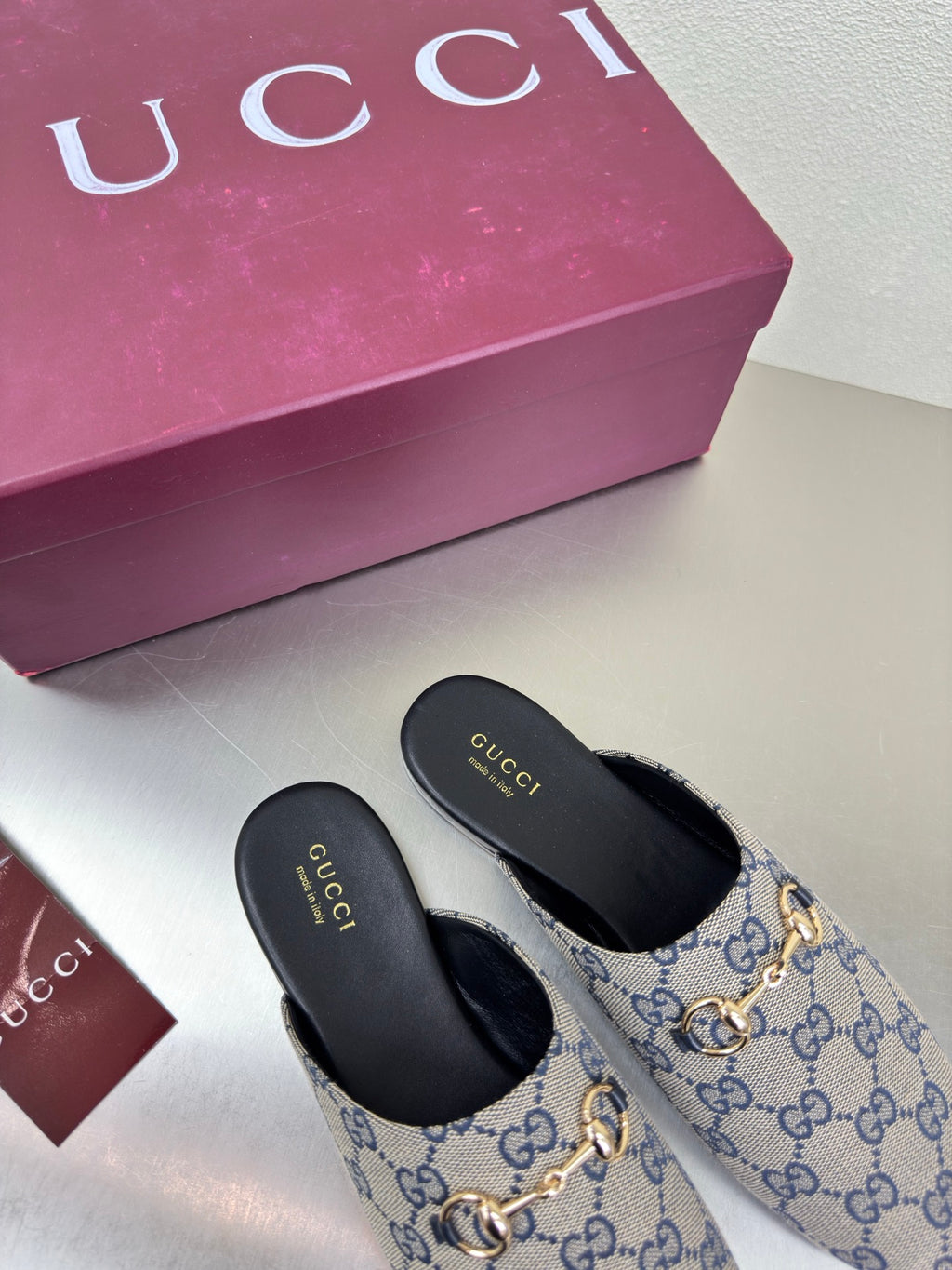 Women’s Gucci GG-pattern slide mules, front view with gold-tone horsebit and black soles