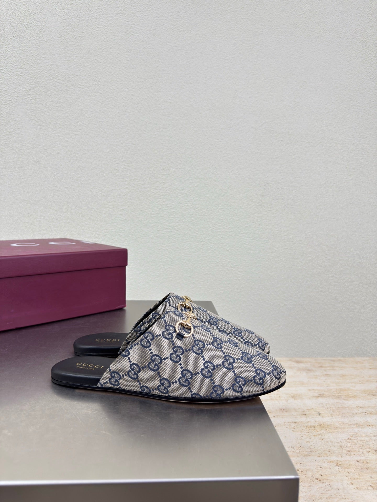 Women’s Gucci GG-pattern slide mules with black sole, side view on display