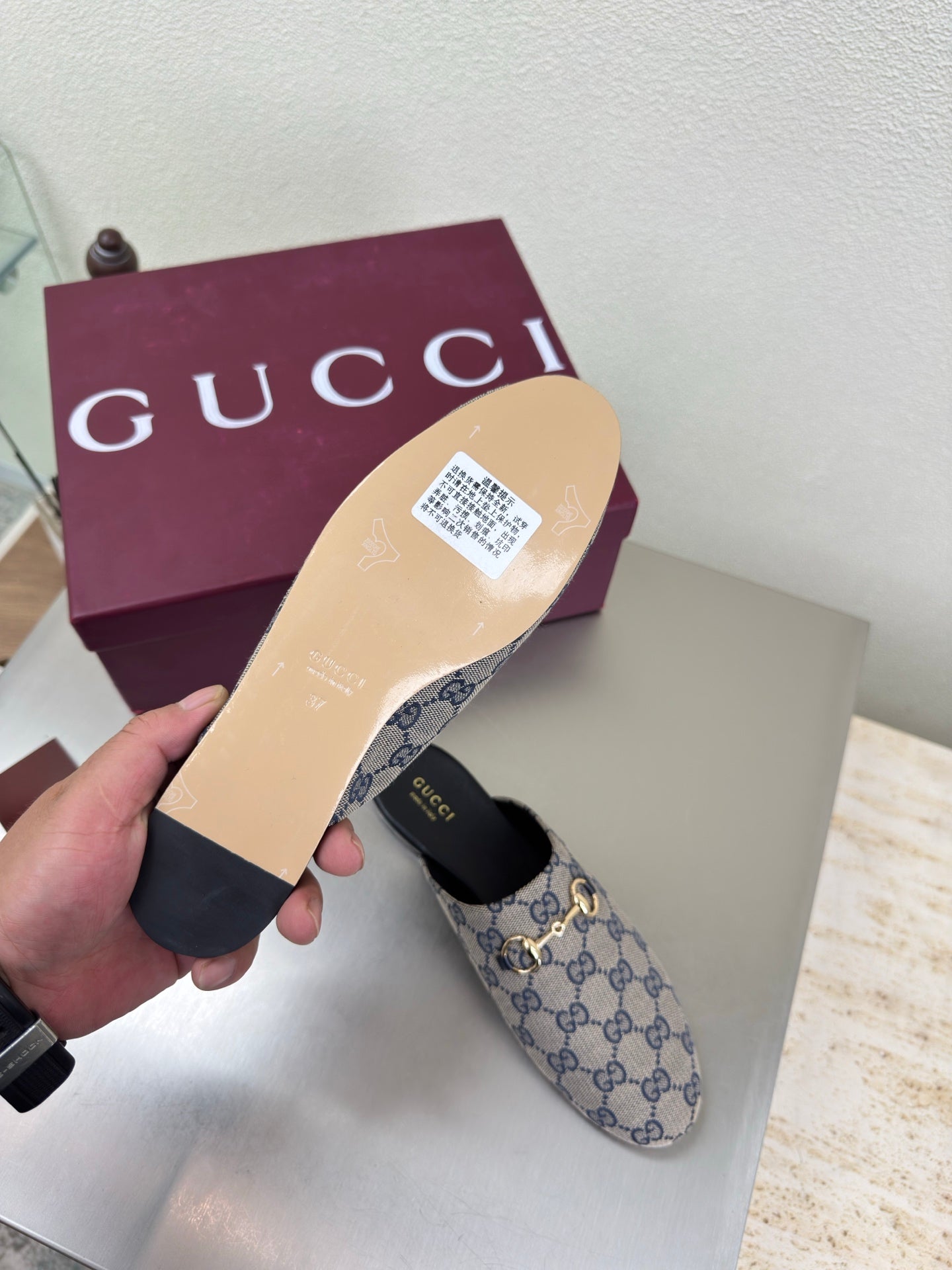 Women’s Gucci slide mules with beige interior lining and GG pattern, held in hand